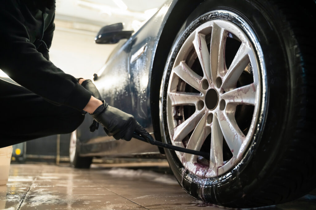 Detailing center worker cleans car wheels with brush. Vehicle wheel rim cleaning process